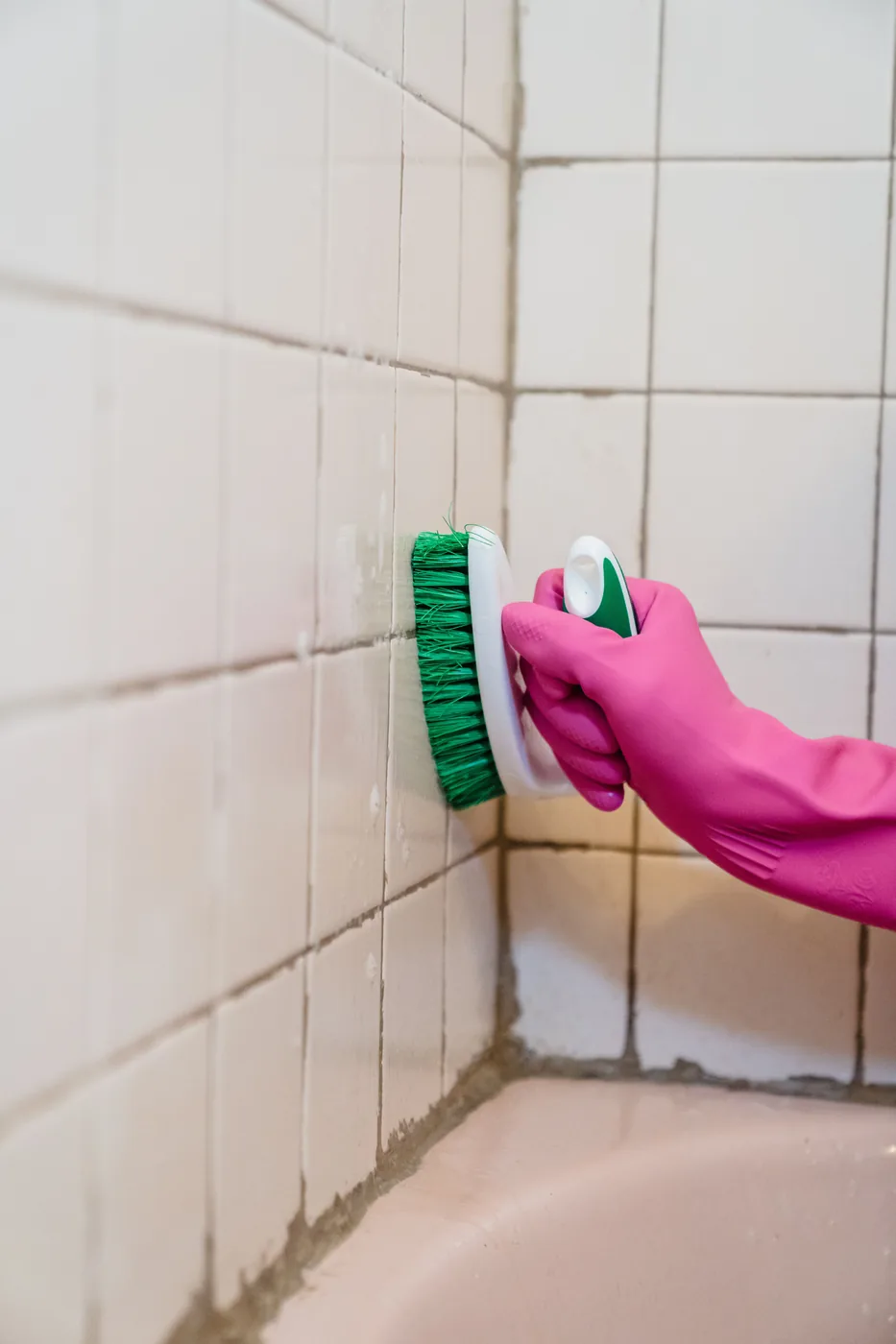 Gloved hand scrubbing tile grout with a cleaning brush