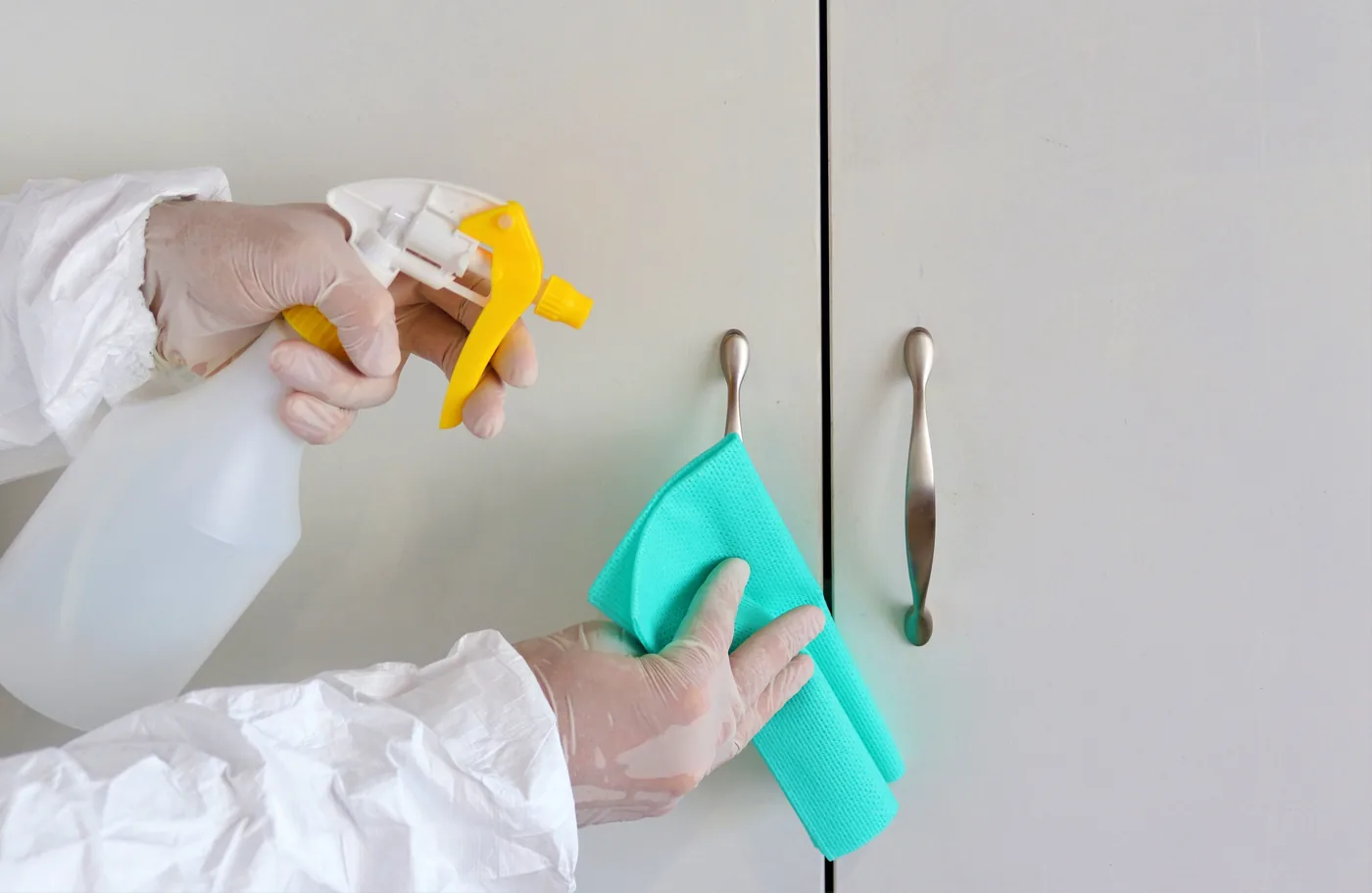 Gloved hands disinfecting cabinet handles with a cloth