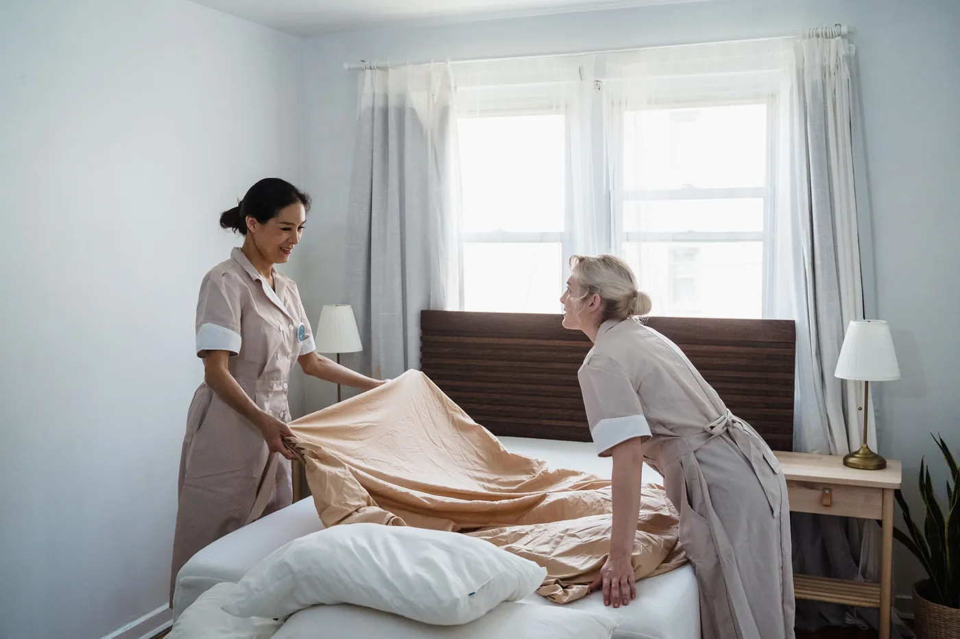 Two cleaners fitting a fresh sheet onto a mattress