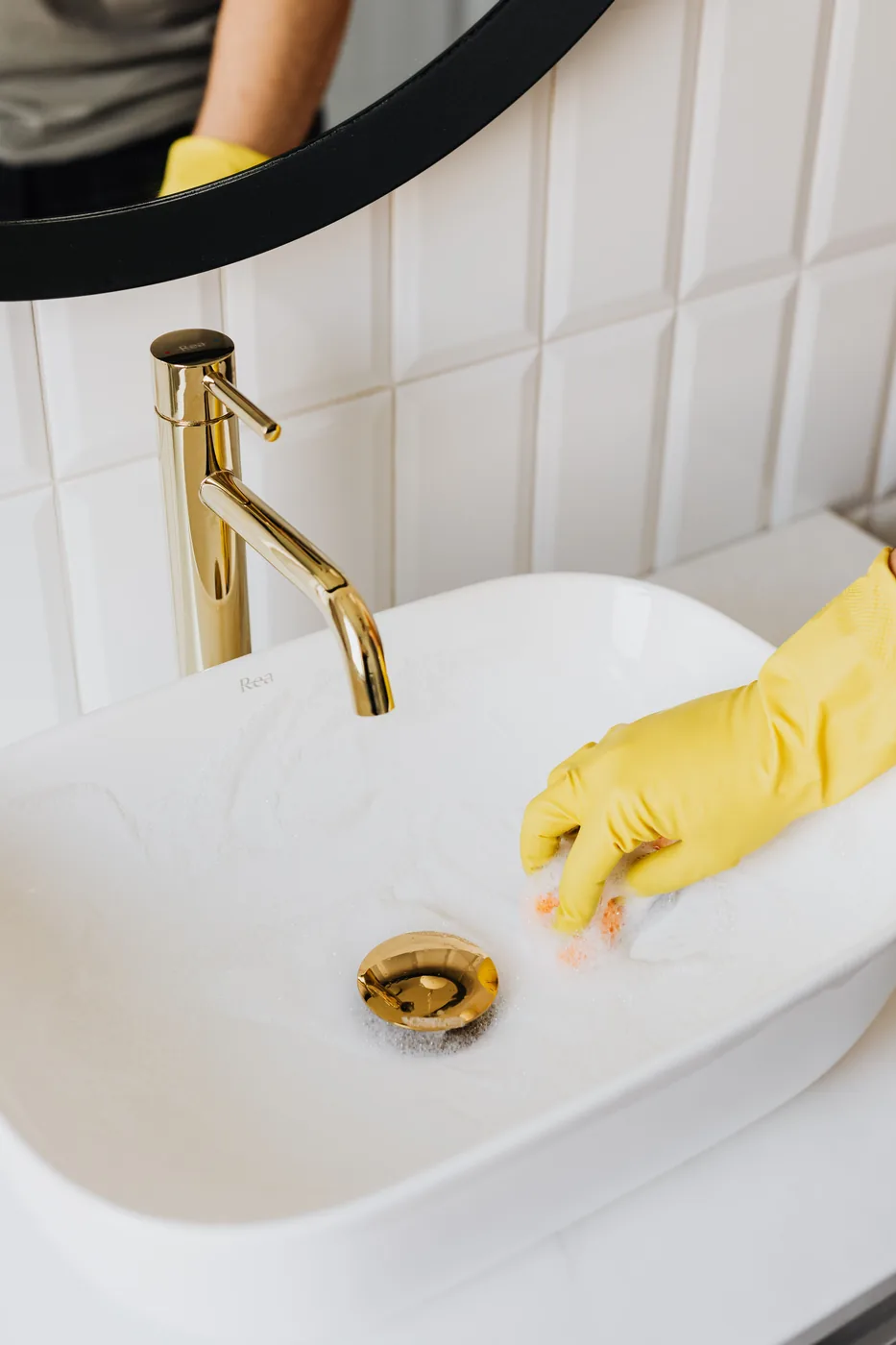 Gloved hand cleaning a bathroom sink and fixtures